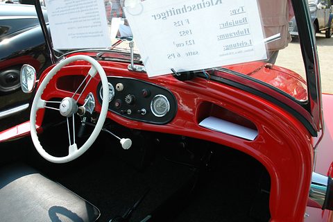Red dashboard with a white steering wheel, gear lever and a small instrument panel, a display card behind. Opens a larger view