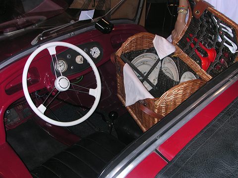 Red cockpit with a white steering wheel, small dials and a wicker picnic basket of plates on the passenger side.