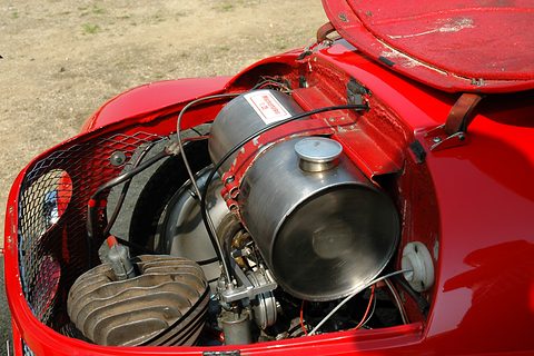 Red bonnet lifted over a finned single-cylinder engine and a polished aluminium fuel tank. Opens a larger view