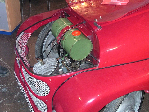 Open red nose revealing a finned engine, a green cylindrical fuel tank and the spare wheel.