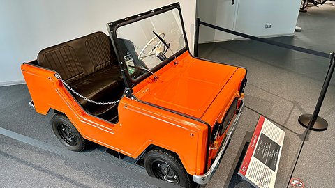 Orange open two-seater with a fold-flat windscreen, black bench seat and chains across the door openings.