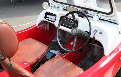 Looking into an open buggy: a thin black wheel, a white dashboard with round dials and tan seats. Opens a larger view