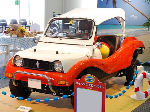 Orange and white doorless buggy with a white canvas top and a grille guard, on a mock beach with a palm tree. Opens a larger view