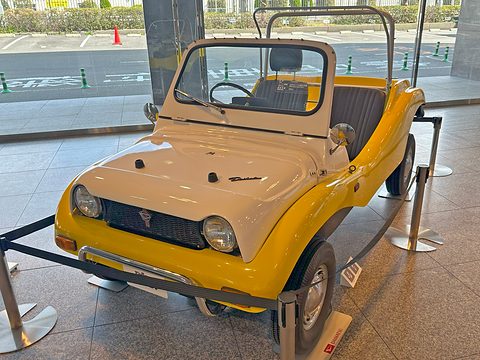 Yellow and white buggy with round headlamps and a grille guard, behind a black rope barrier.