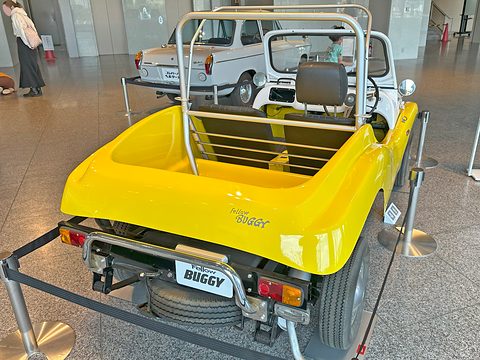 Rear view of a yellow open buggy with a chrome roll bar, a spare wheel and a BUGGY plate. Opens a larger view