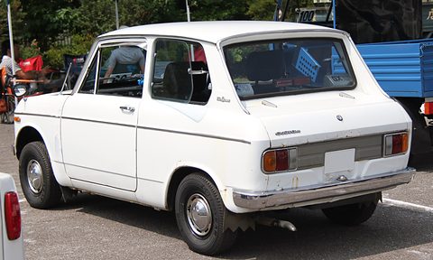 Rear three-quarter of a white boxy saloon with wide rectangular tail lamps and a chrome bumper. Opens a larger view