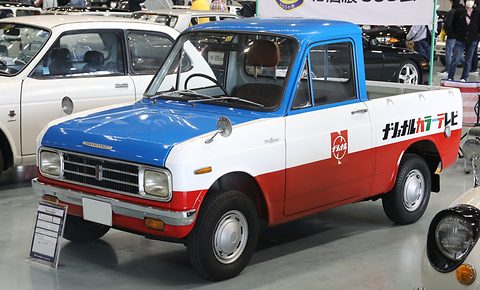 Pickup in red, white and blue with Japanese lettering on the bed side, parked among other cars indoors.