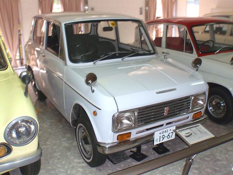 White boxy small saloon with rectangular headlamps and a chrome grille, beside a museum placard. Opens a larger view