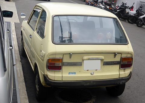 Rear view of a cream two-door hatchback by a kerb, motorcycles parked ahead of it. Opens a larger view