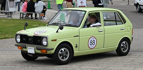 Lime-green four-door hatchback with a round number 88 on the door, passing a grassy area with spectators.