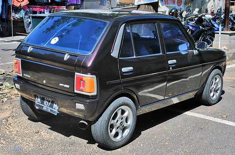 Rear three-quarter of a dark brown four-door hatchback with alloy wheels, leaves on the road. Opens a larger view