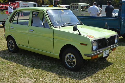 Lime-green four-door hatchback on grass, a blue truck and visitors behind. Opens a larger view