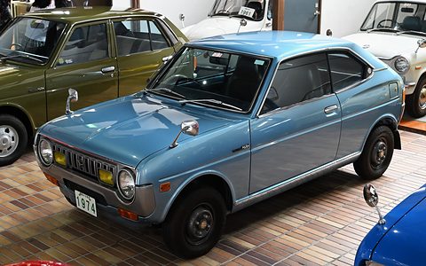 Pale blue pillarless coupé on a wooden parquet floor, an olive saloon behind. Opens a larger view