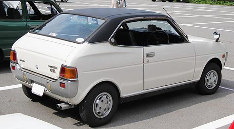 Rear three-quarter of a white coupé with a black vinyl roof, twin exhausts and amber tail lamps. Opens a larger view