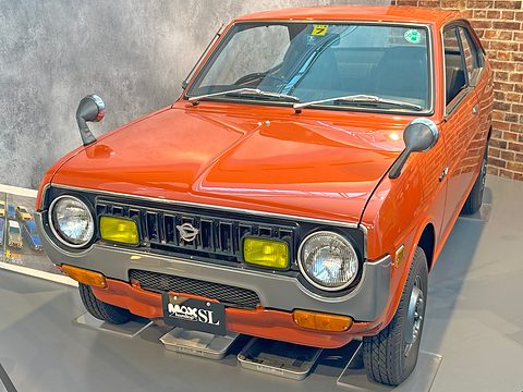 Orange coupé seen from the front with a black grille, yellow fog lamps and round headlamps. Opens a larger view