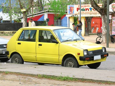 Yellow small four-door hatchback parked by a kerb in front of a colourful sign.