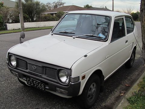 White two-door hatchback with round headlamps and a black grille, parked on a suburban street. Opens a larger view