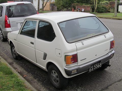 Rear three-quarter of a white two-door hatchback parked at a kerb beside a silver car. Opens a larger view