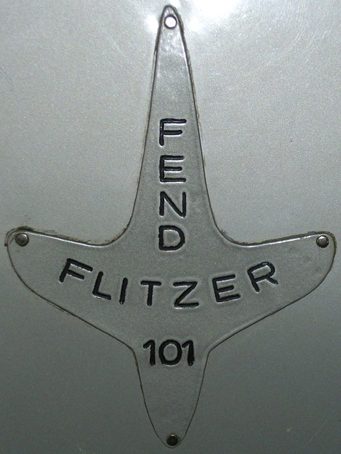 Close-up of an aluminium four-pointed badge riveted to silver paint, with engraved black lettering. Opens a larger view