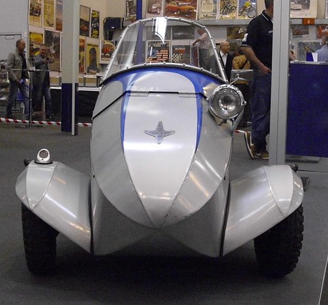 Silver and blue open single-seater from the front, with a separate headlamp and a star-shaped nose badge. Opens a larger view