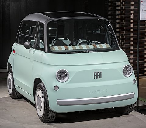 Mint-green rounded two-seater with chrome-ringed headlamps, a striped dashboard roll and white wheel covers on a show floor.