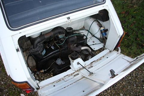 Open rear engine compartment of a white car showing a black engine, air ducting and a white fan housing. Opens a larger view
