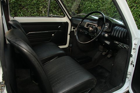 Black vinyl front seats, a black steering wheel on the right and black floor mats seen through an open white door. Opens a larger view