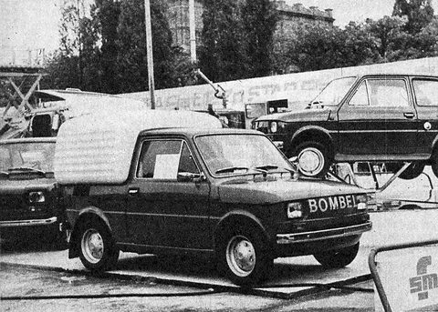 A dark small pick-up with a canvas tilt over its bed and BOMBEL lettering on its nose, a 126p raised on a stand behind. Opens a larger view