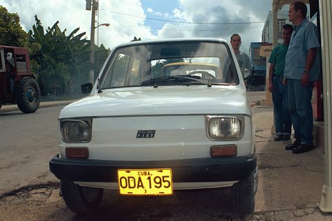 Head-on view of a white small car with black bumpers and a yellow CUBA plate, three men standing beside it. Opens a larger view