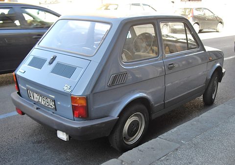 Rear three-quarter of a blue-grey small car with black bumpers, slotted engine lid and a 126 FSM badge. Opens a larger view