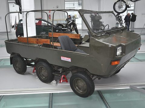 Olive-green open six-wheeled vehicle with a boat-like hull, roll bars and two seats on a museum floor. Opens a larger view