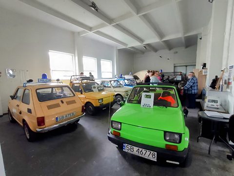 Museum room with a bright green 126p in front and a row of yellow, cream and blue police-light cars behind. Opens a larger view