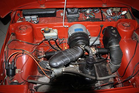 Red engine bay with a small engine, black air ducts, a brake fluid reservoir and wiring. Opens a larger view