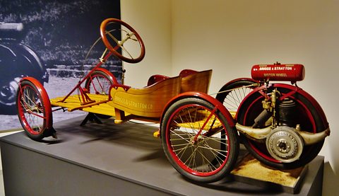 Rear view of a wooden buckboard with red wheels, the engine-carrying fifth wheel and a red Briggs & Stratton tank in the foreground.