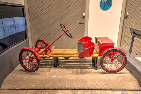 A red-wheeled slatted wooden buckboard with a red seat box and battery box, its steering column raked forward. Opens a larger view