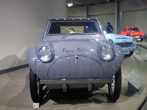 Front view of a small grey car with two round headlamps on bulbous wings and a slotted oval nose panel.