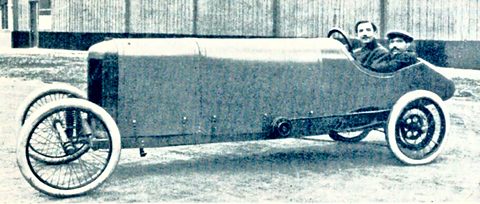 Side view of a long, slab-sided racing cyclecar with wire wheels, two men in caps sitting low at its tail. Opens a larger view