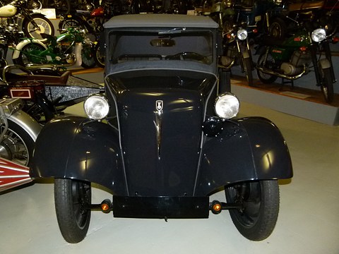 Front of a black small car: rounded bonnet, two round headlamps, black wings and a grey hood. Opens a larger view