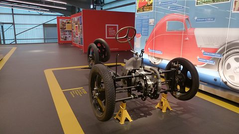 Rolling chassis on yellow stands: engine between wide-set front wheels, a backbone tube and closely set rear wheels.