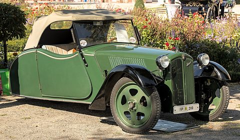 Side view of a green open car with a beige hood whose body tapers to a narrow tail, flowers behind. Opens a larger view