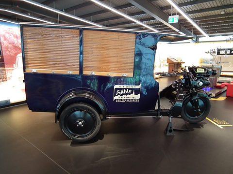 Three-wheeled delivery van with a motorcycle front end and a blue box body with wooden slatted sides.
