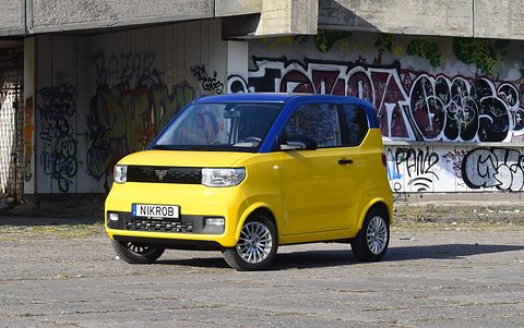 Yellow and blue boxy city car on a concrete yard in front of a graffiti-covered building.
