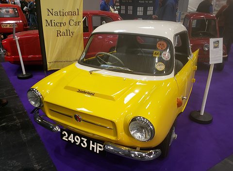 Yellow small car with a white roof on a purple carpet beside a National Micro Car Rally banner. Opens a larger view