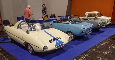 Row of three small cars on a blue carpet, a white racer with a blue stripe in front. Opens a larger view