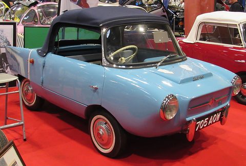 Pale blue two-seater with a black fabric hood and whitewall tyres on a red carpet. Opens a larger view