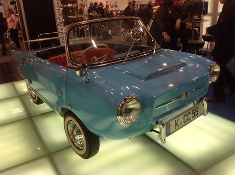 Pale blue open two-seater on a glowing glass floor, seen from the front left. Opens a larger view