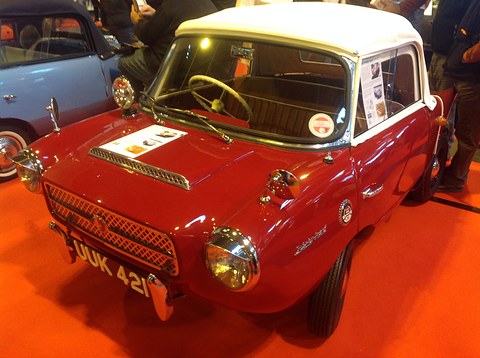 Red two-seater with a white hardtop on an orange show carpet, seen from the front left
