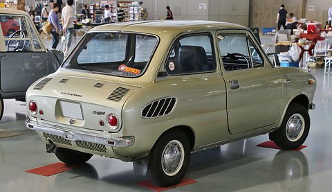 Rear three-quarter of a pale gold-green saloon with oval side vents, on a red mat. Opens a larger view