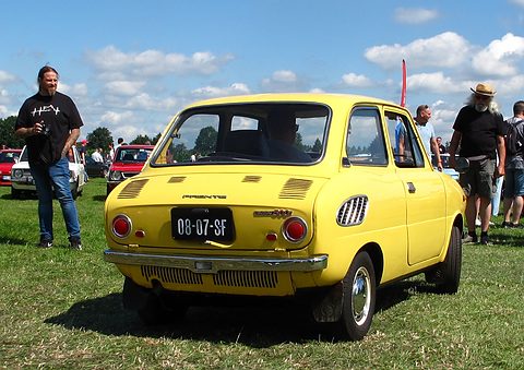 Rear view of a yellow small saloon on grass, two men standing on either side. Opens a larger view