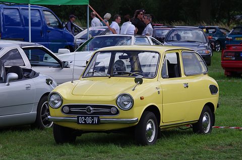 Yellow small saloon on grass among white and silver cars, visitors and tents behind. Opens a larger view